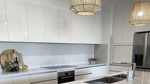 Et moderne køkken med hvide skabe, en stor ø med barstole og hængende lamper.