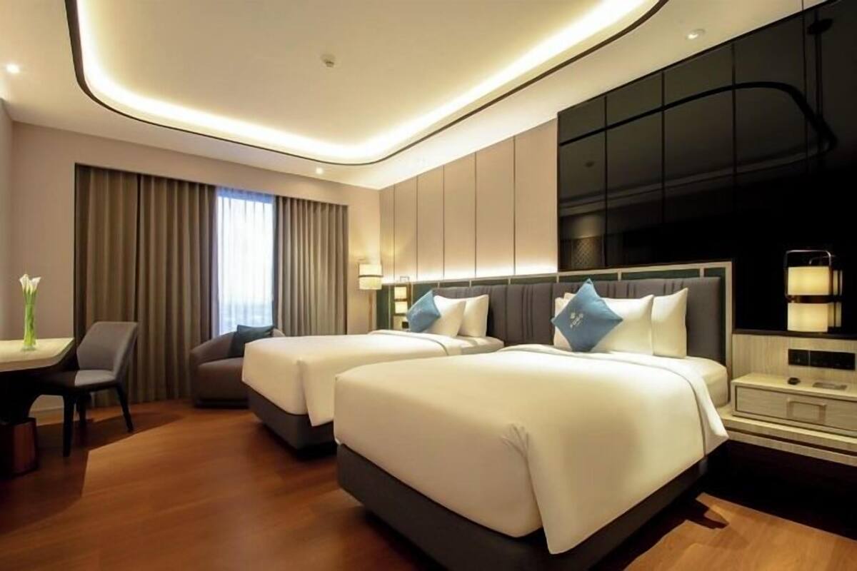 A modern hotel room with two beds, a desk, and a large window with curtains.