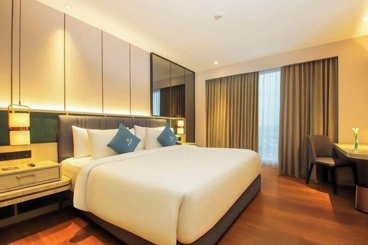 A modern hotel room with a large bed, a desk, and a chair.