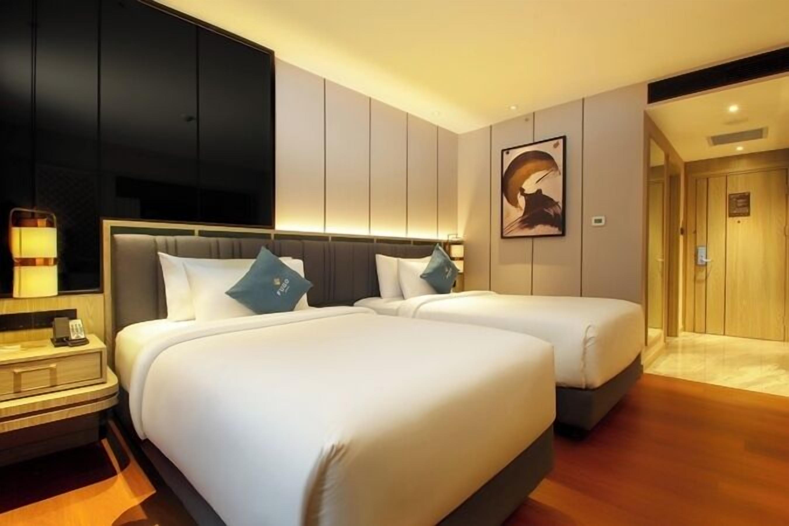 Habitación de hotel con dos camas, un televisor, una mesita de noche y un cuadro en la pared.