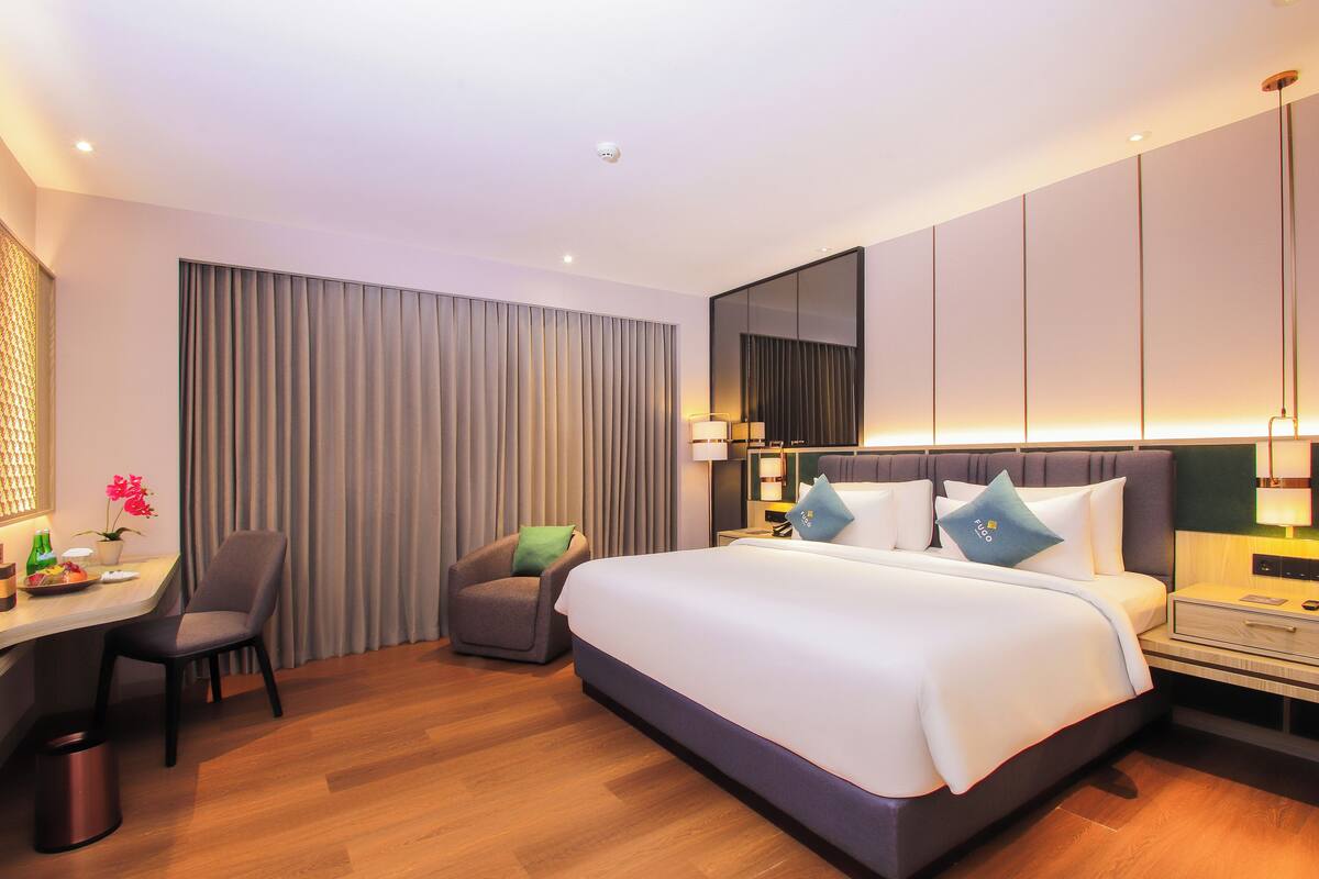 A modern hotel room with a large bed, a desk, a chair, and a small table.