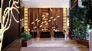 Un vestíbulo moderno de hotel con un mostrador de recepción, una escalera y una zona de espera con una pantalla grande.