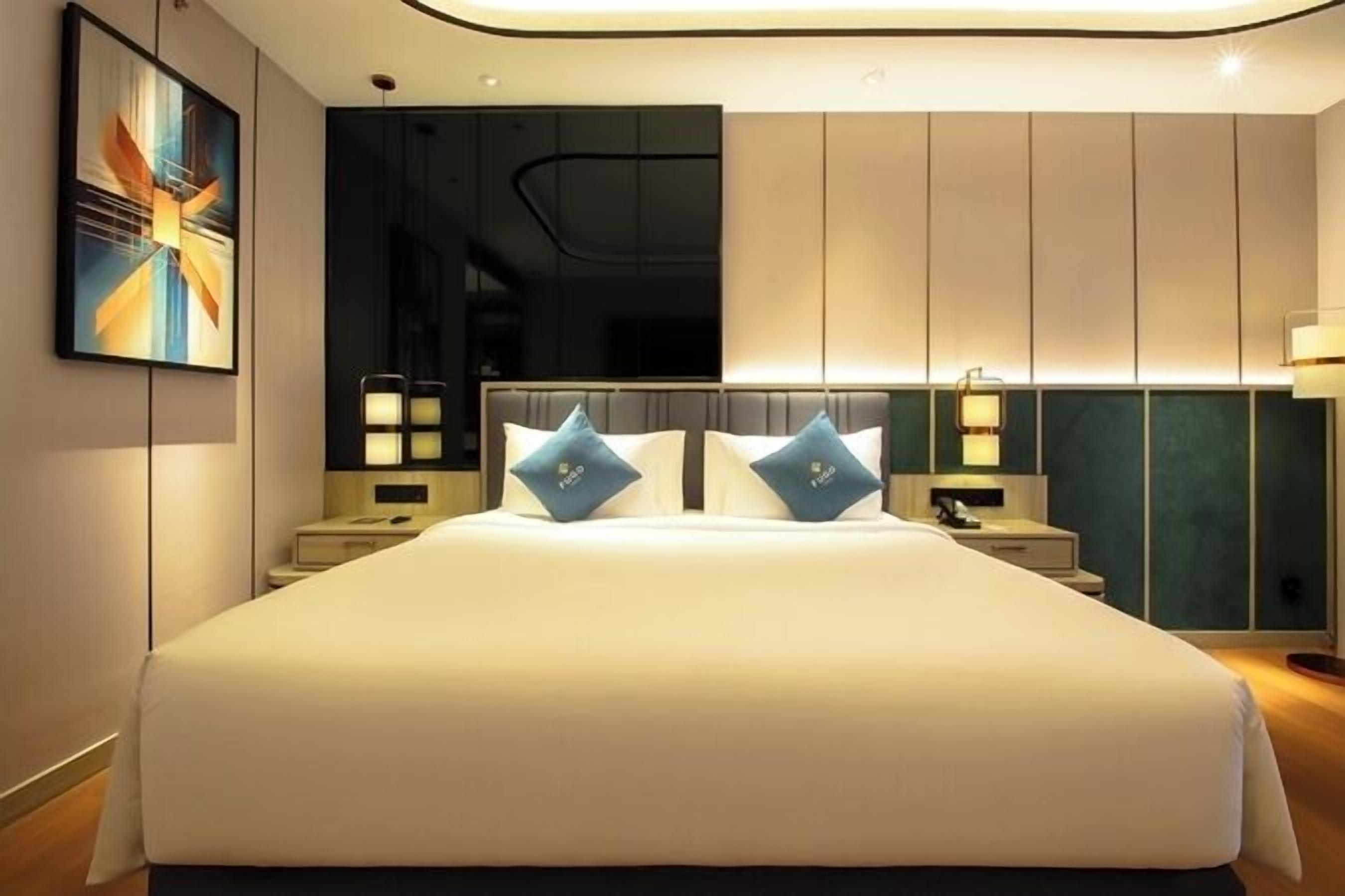 Ein modernes Hotelzimmer mit einem großen Bett, zwei Nachttischen und einem an der Wand montierten Fernseher.