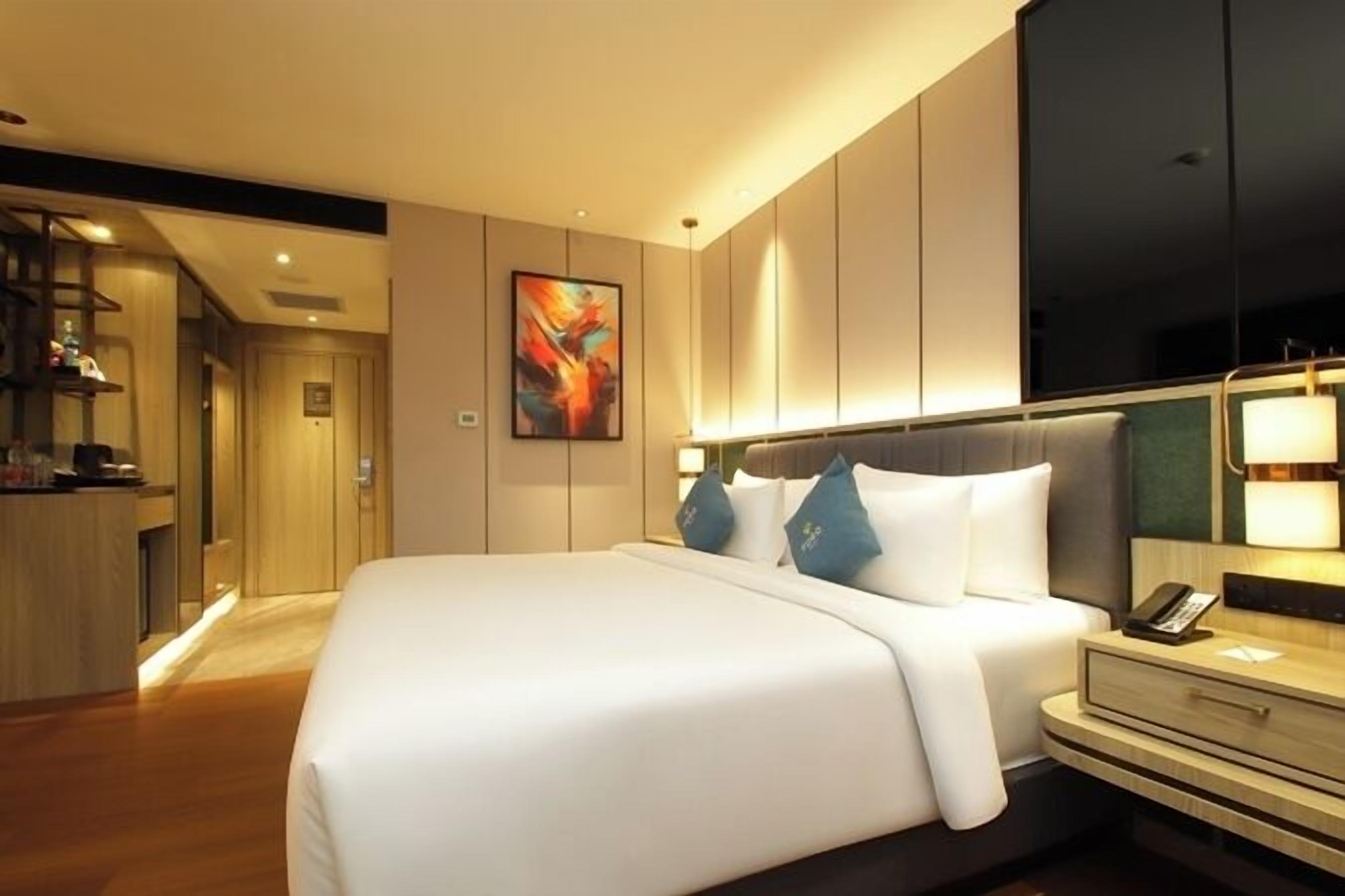 Una habitación de hotel moderna con una cama grande, una mesita de noche y un televisor montado en la pared.