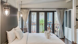 A hotel room with a large bed, two bedside lamps, a view of the outside balcony, and a door leading to another room. - Priya Boutique House (Bangkok)