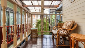 A covered porch with wicker furniture, a wooden railing, and a view of greenery outside. - Priya Boutique House (Bangkok)