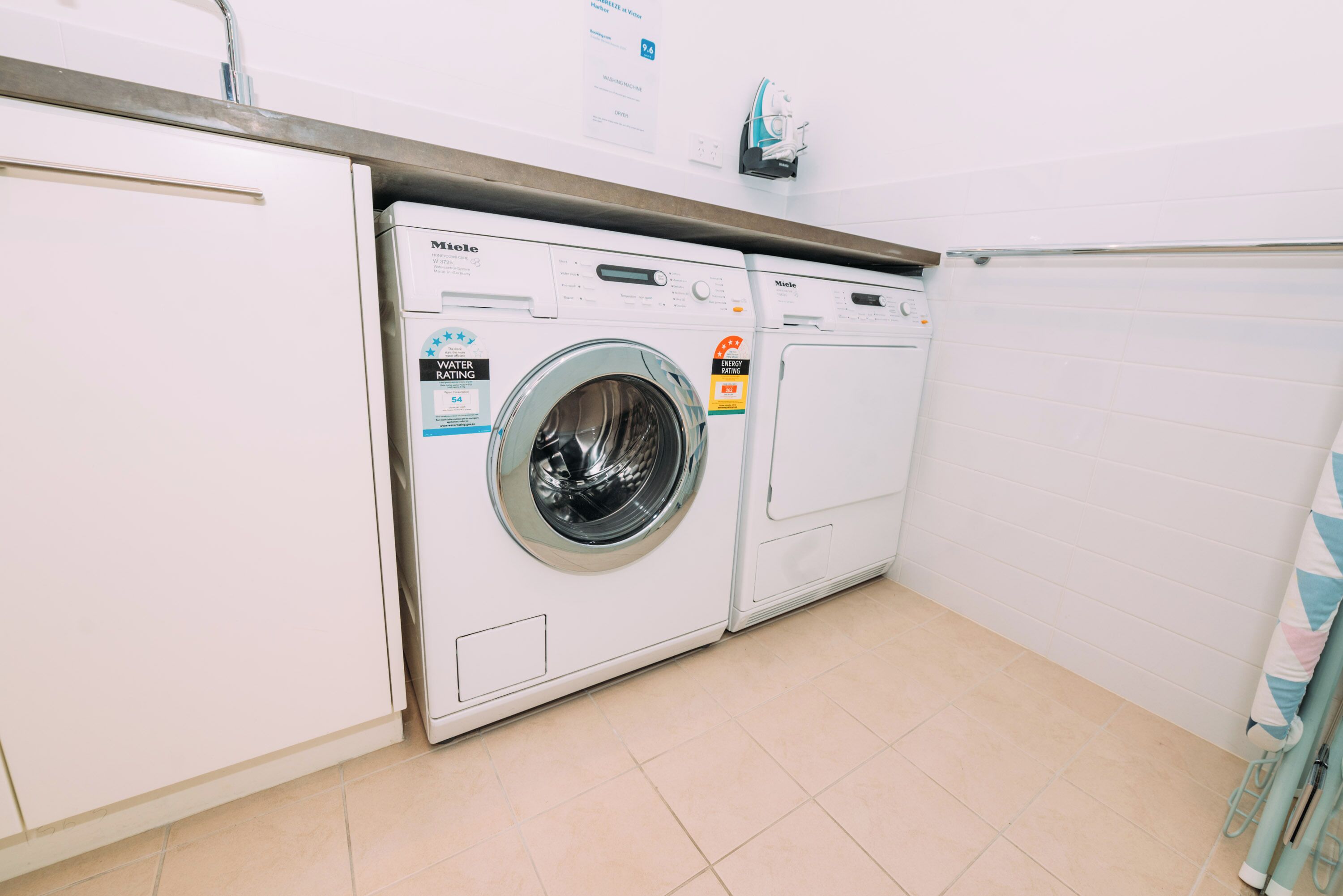 A laundry room with two front-loading washing machines, a metal towel rack, and a tiled floor.