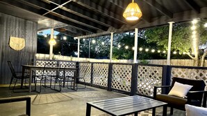 An outdoor patio area with a table and chairs, a hanging light fixture, and a wooden fence. - Trendy&Cute4BR+Pool-NearStMary’sUniversity&DTSA! (San Antonio)