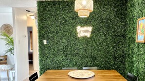A dining area with a wooden table and chairs, a green wall with a 'Buenos Vibes' sign, and a hanging light fixture. - Trendy&Cute4BR+Pool-NearStMary’sUniversity&DTSA! (San Antonio)