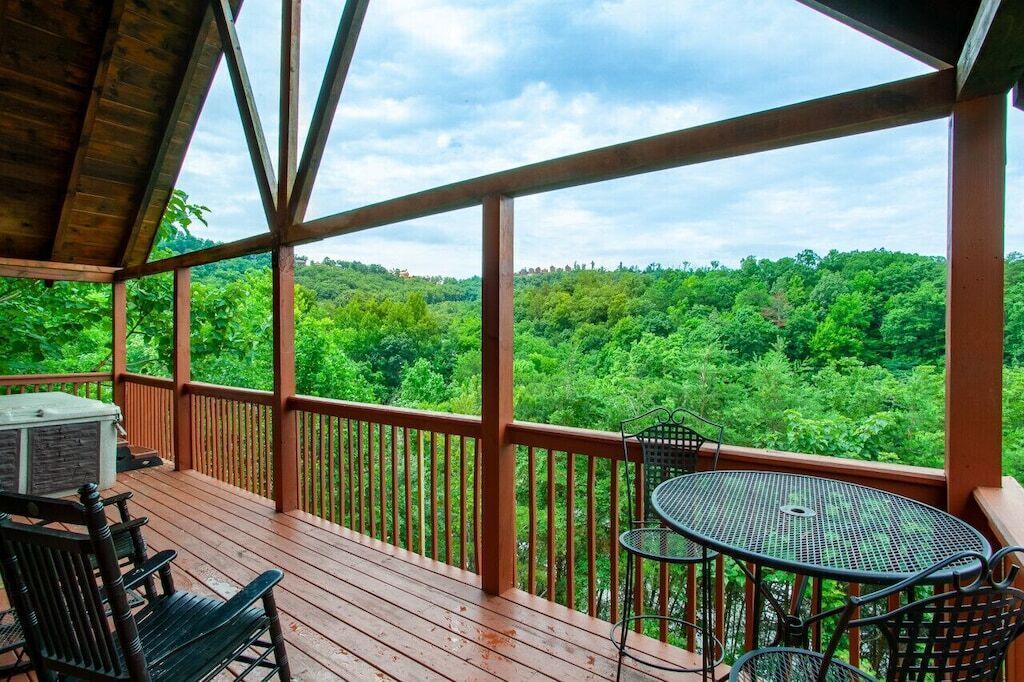 A wooden deck with a table and chairs, overlooking a lush green forest.