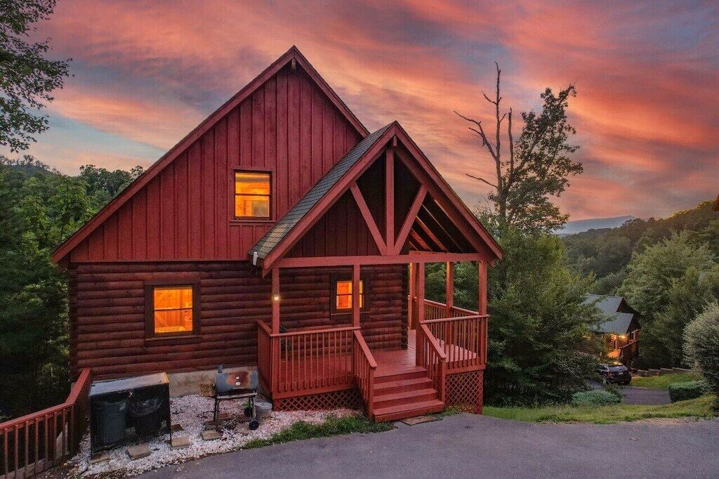 Une cabane en rondins avec un porche et une cheminée, entourée d’arbres.
