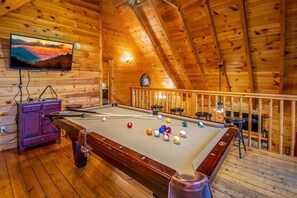 Een houten interieur met een pooltafel, een aan de muur bevestigde televisie en een klok.