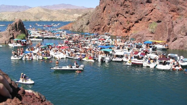 Un puerto deportivo concurrido, con numerosas embarcaciones amarradas, rodeado de acantilados rocosos.