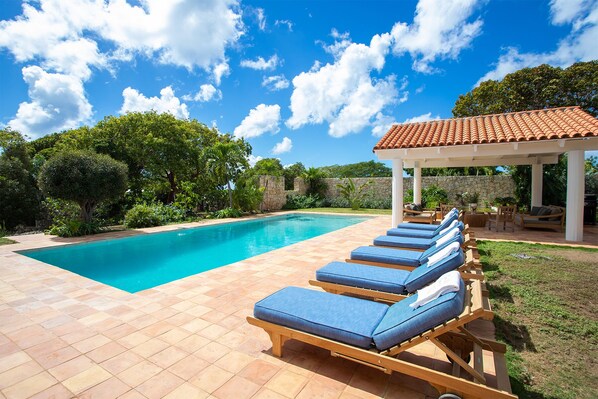 A swimming pool with blue lounge chairs and a covered seating area.