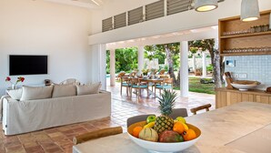 A modern living room with a sofa, a dining area with a table and chairs, a fruit bowl, and a kitchen area with a countertop and cabinets. - Jasper -20% Low Season Promo | Ocean Front - Located in  Stunning Simpson Bay with Private Pool (Marigot)