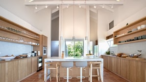A modern kitchen with wooden cabinets, a central island with bar stools, and a large window providing a view of greenery. - Jasper -20% Low Season Promo | Ocean Front - Located in  Stunning Simpson Bay with Private Pool (Marigot)