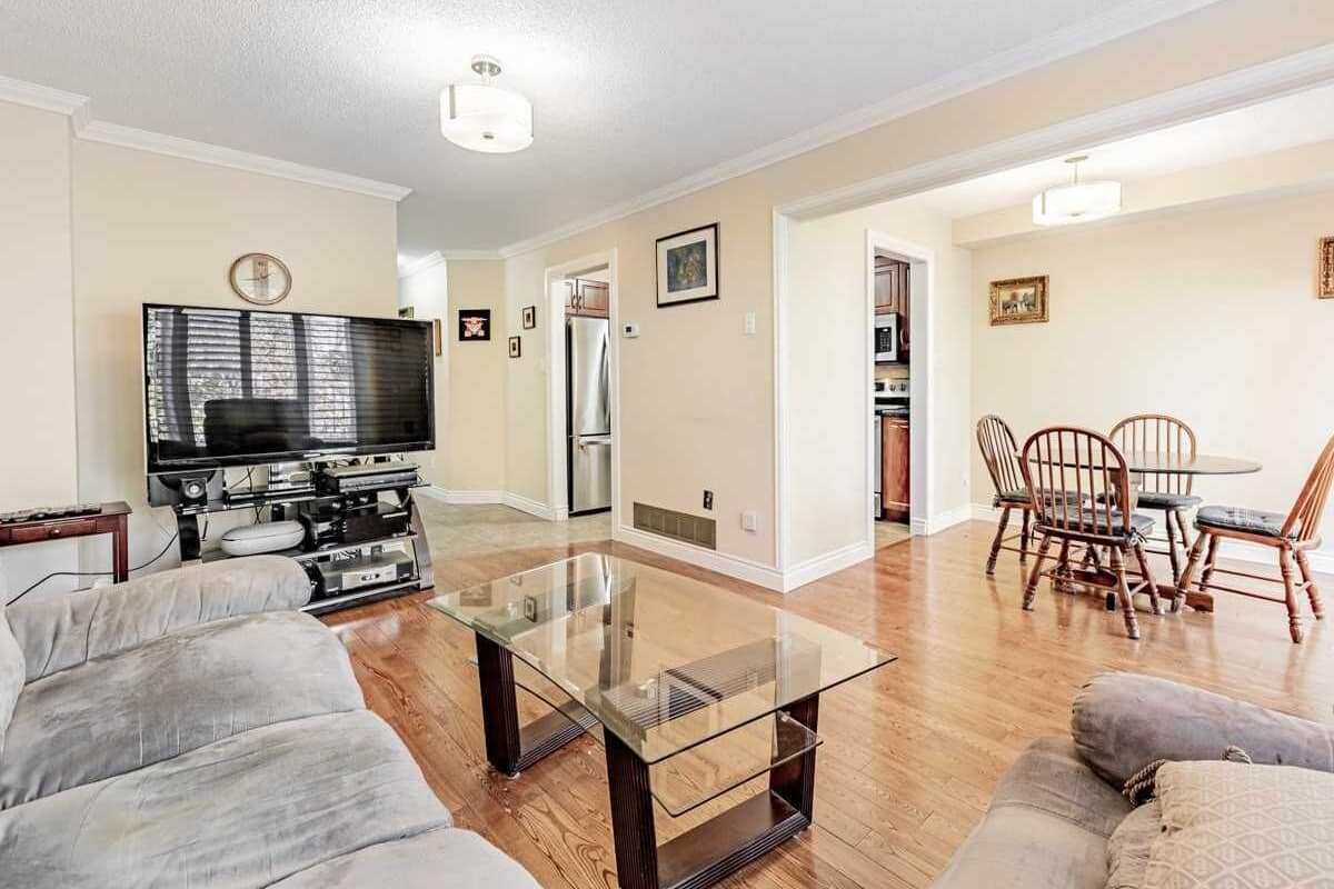 A living room with a glass coffee table, a sofa, a TV, and a dining area with wooden chairs and a table.