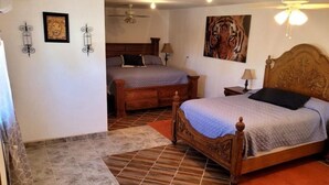 Une chambre avec deux lits, une tête de lit en bois, un tableau représentant un tigre et un ventilateur de plafond.