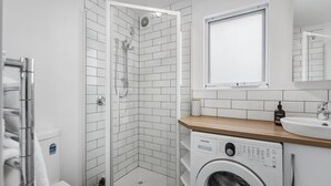 Moderni kylpyhuone, jossa on suihku, pesukone ja pesuallas.