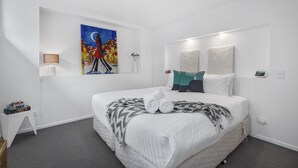 Moderni hotellihuone, jossa on suuri sänky, taulu seinällä, pieni sivupöytä ja yöpöytälamppu.