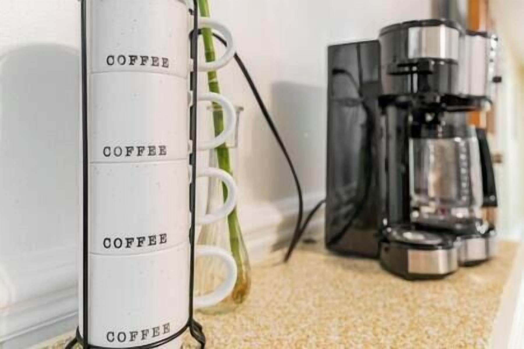 Une machine à café blanche, sur laquelle est inscrit le mot «COFFEE», est placée à côté d’une plante verte.