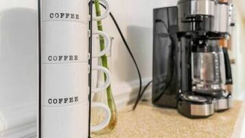 Une machine à café blanche, sur laquelle est inscrit le mot «
COFFEE
», est placée à côté d’une plante verte.