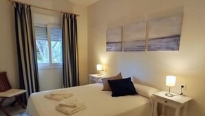 A hotel room with a neatly made bed, two bedside tables with lamps, a chair, and a window with curtains. - Pool and terrace Santa Catalina beach (El Puerto de Santa María)