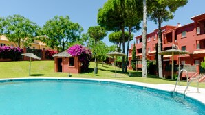 A swimming pool with a lifeguard tower, surrounded by red buildings and green trees. - Pool and terrace Santa Catalina beach (El Puerto de Santa María)