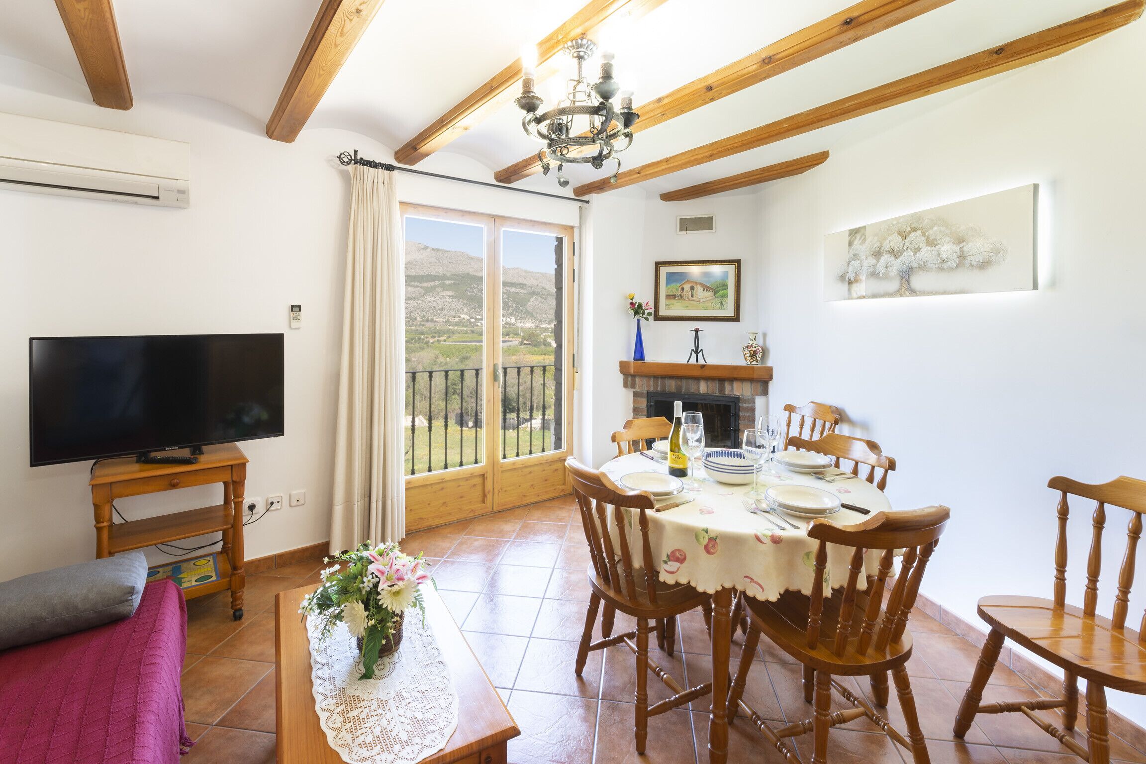 Un coin repas avec une table dressée pour quatre personnes, des chaises en bois, un téléviseur et une cheminée.