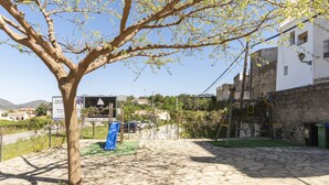 Un cortile lastricato con un albero, un'area giochi e un edificio con un cartello.