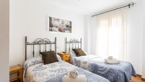 Una camera da letto con due letti, ognuno con una coperta a fantasia, un comodino, una sedia di legno e un quadro appeso al muro.