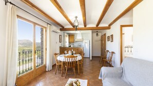 Zona pranzo con tavolo e sedie in legno, cucina sullo sfondo e balcone con vista sulla campagna.