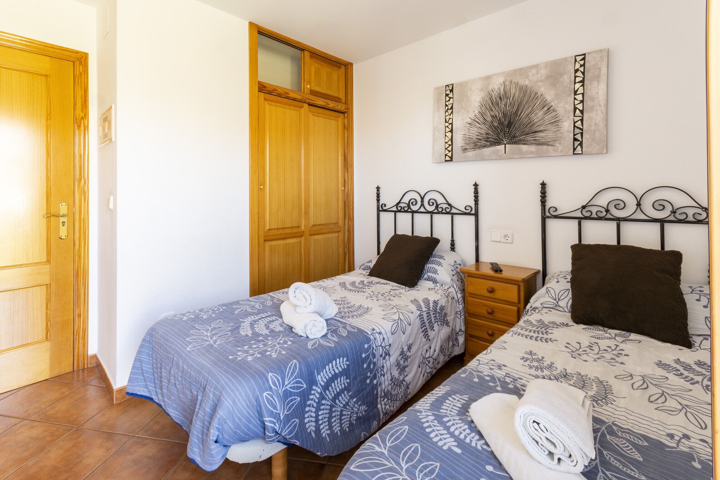 A bedroom with two beds, wooden wardrobe, and artwork on the wall.