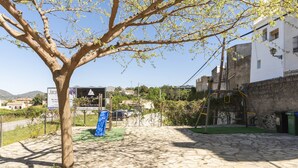 A courtyard with a tree, a playground, and a building with a sign. - CARREBAIX V - Cosy studio with free WiFi. (Orba)
