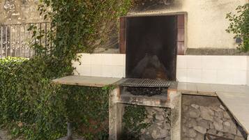 A stone-built outdoor grill area with a tiled wall and a metal gate.