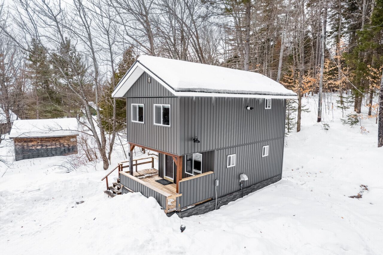 A two-story cabin with a snow-covered roof, surrounded by trees.