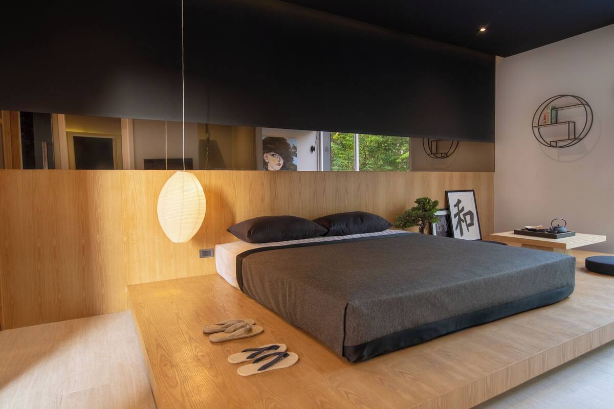 Un dormitorio moderno con una cama plataforma de madera, una lámpara colgante y vistas a la vegetación exterior.