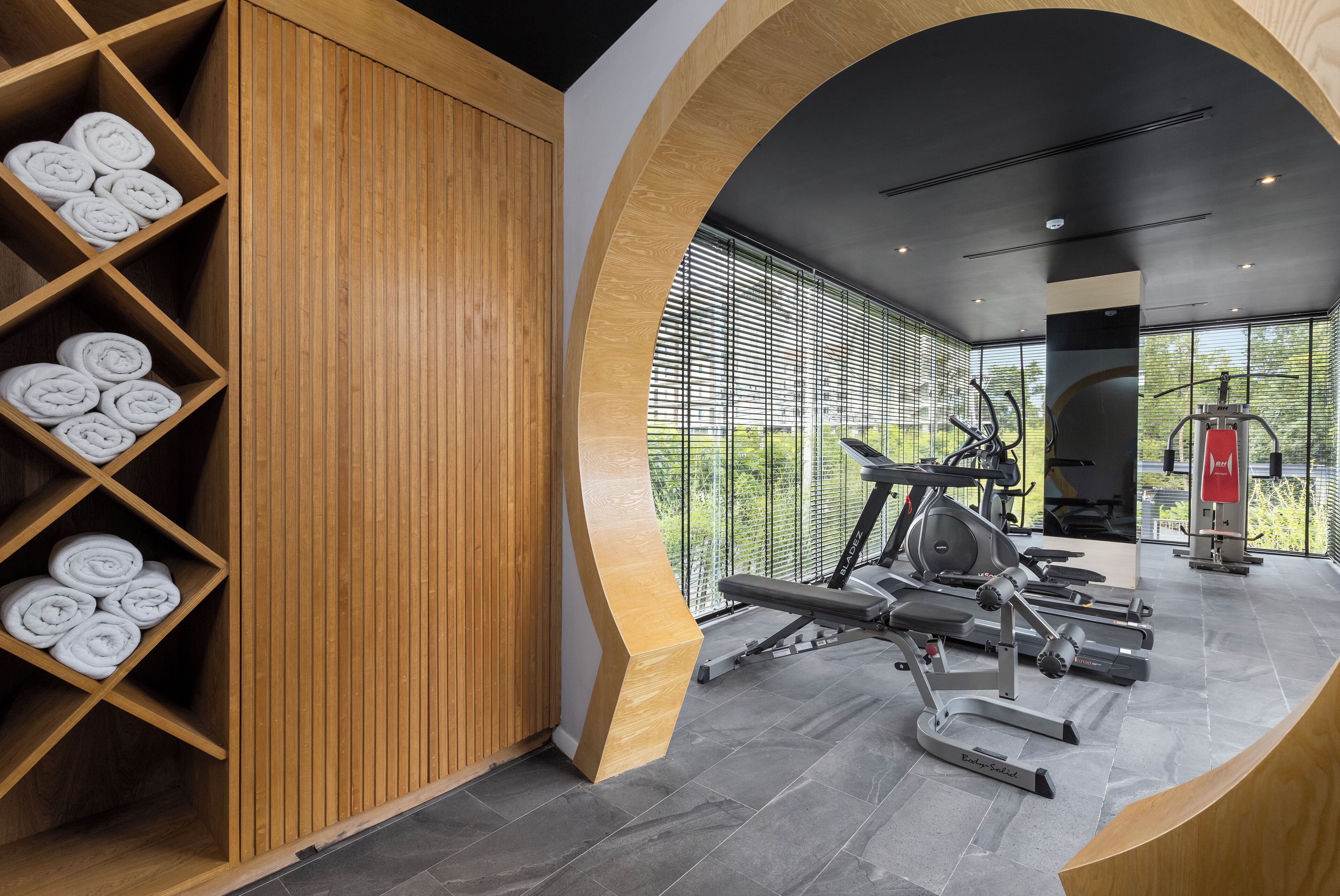 Un gimnasio moderno con taquillas de madera, equipo de ejercicio y amplias ventanas que ofrecen vistas a zonas verdes.