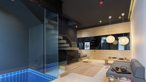 A modern living room with a glass wall, a staircase, a sofa, and a coffee table. - Villoft Zen Living (Choeng Thale)
