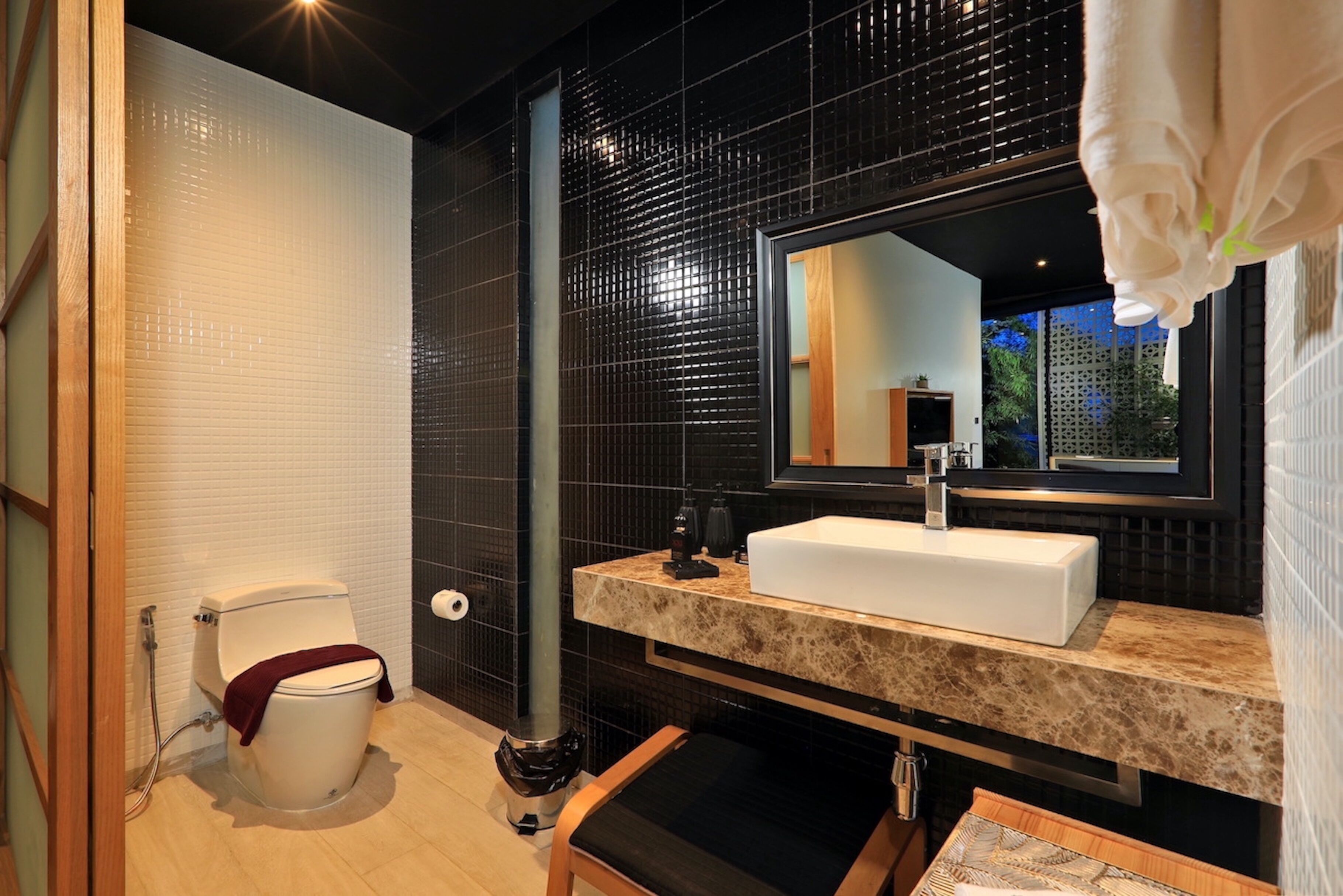 A modern bathroom with a white toilet, a sink with a marble countertop, and a large mirror.