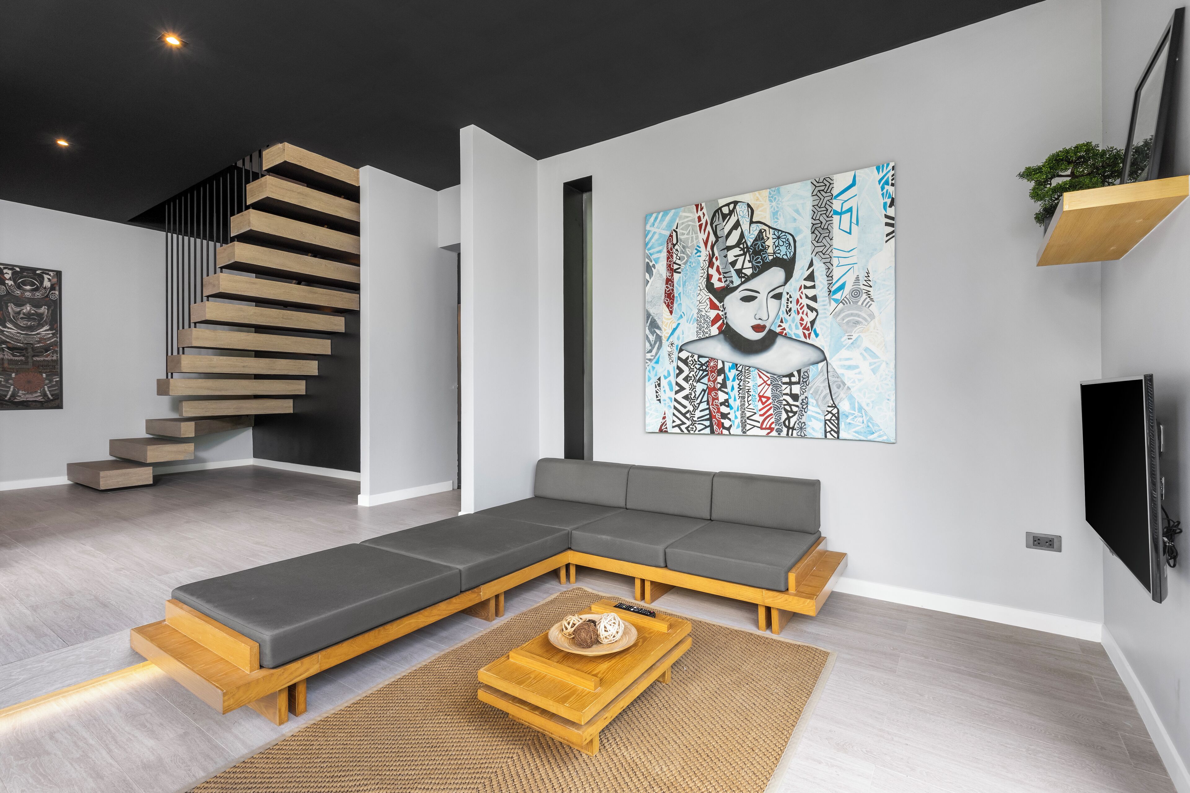 A modern living room with a sectional sofa, a wooden coffee table, a staircase, and a large abstract painting on the wall.