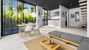 A modern living space with a dining area, a kitchen, and a seating area with a sofa and a coffee table. - Villoft Zen Living (Choeng Thale)