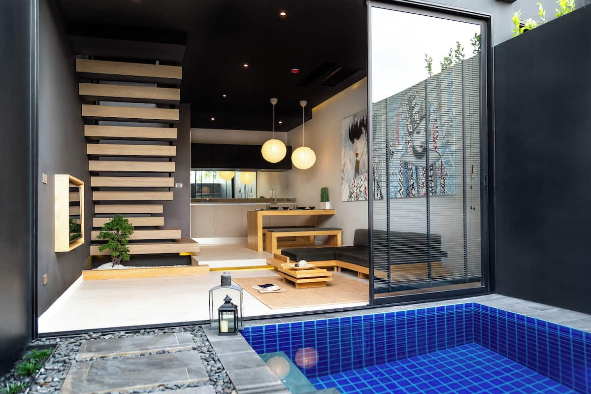 Un interior moderno con una escalera, muebles de madera, un pequeño jardín interior y una zona de piscina con azulejos azules.