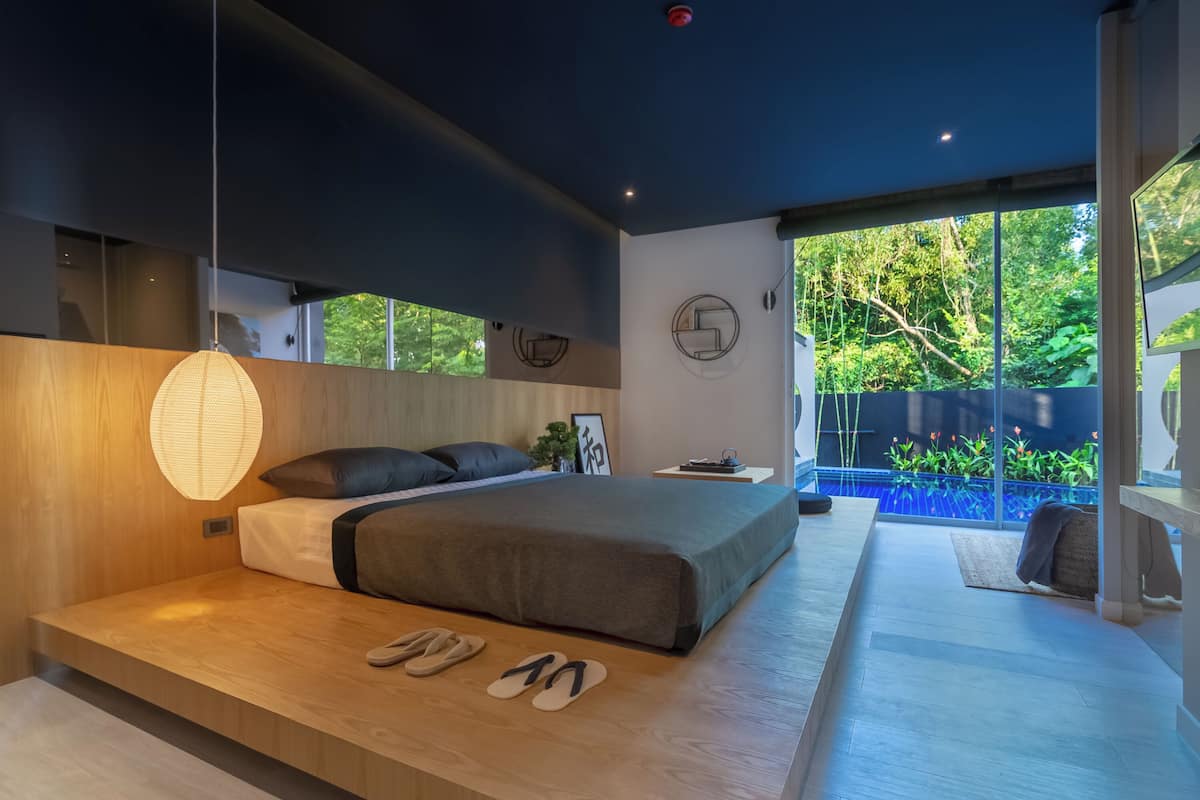 Un dormitorio moderno con una cama grande, una mesita de noche, una lámpara colgante y vistas a una piscina.