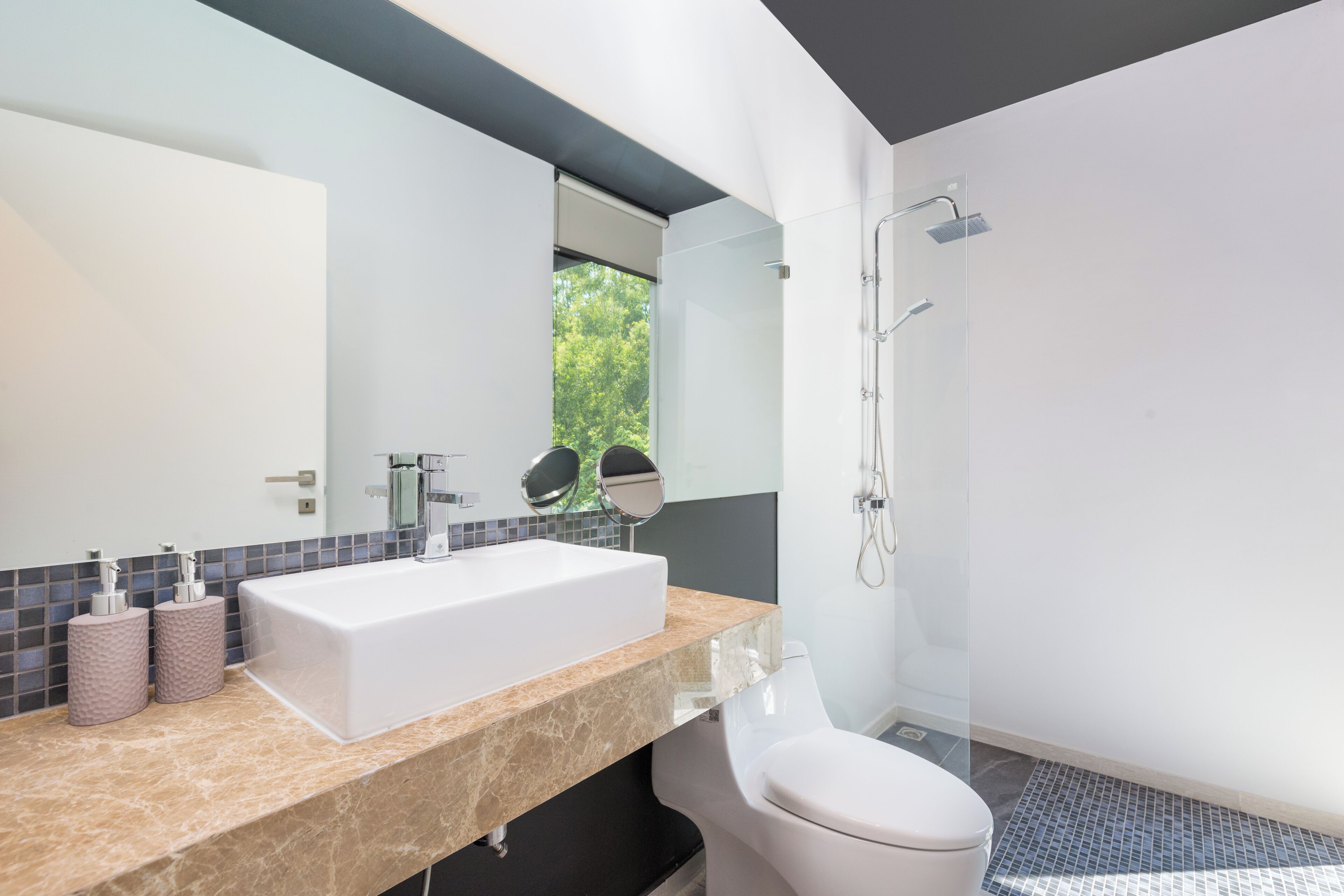 Un baño moderno con un lavamanos grande de color blanco, un inodoro y una ducha con cerramiento de vidrio.