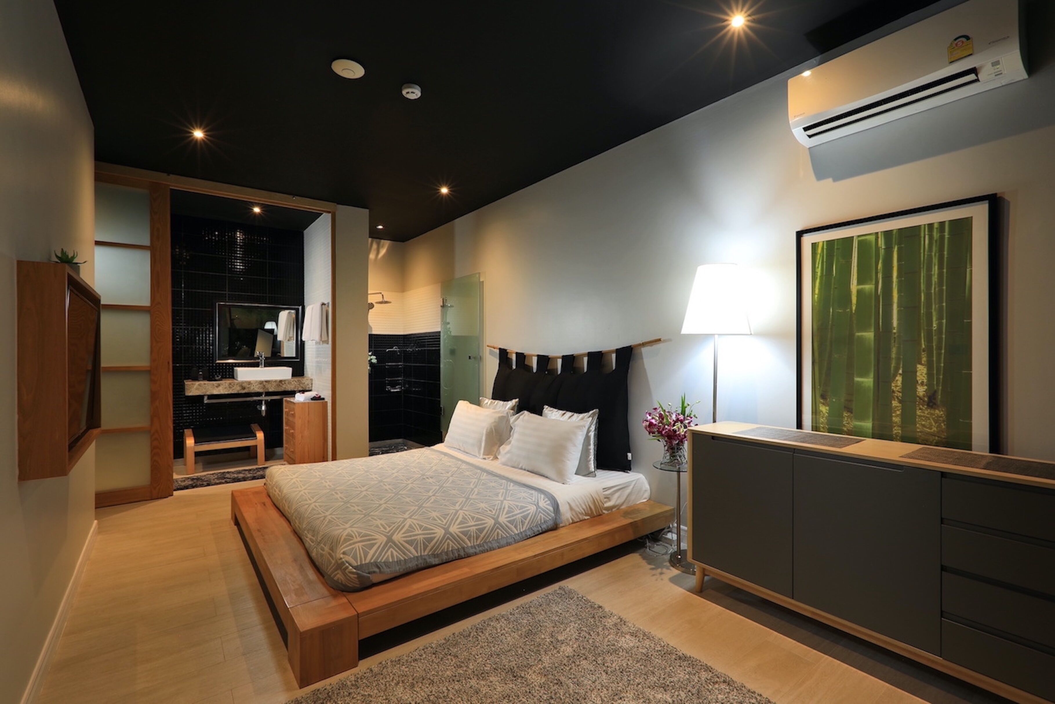 Un dormitorio moderno con una cama grande, una mesita de noche con lámpara, un armario y un baño visible a través de una puerta abierta.