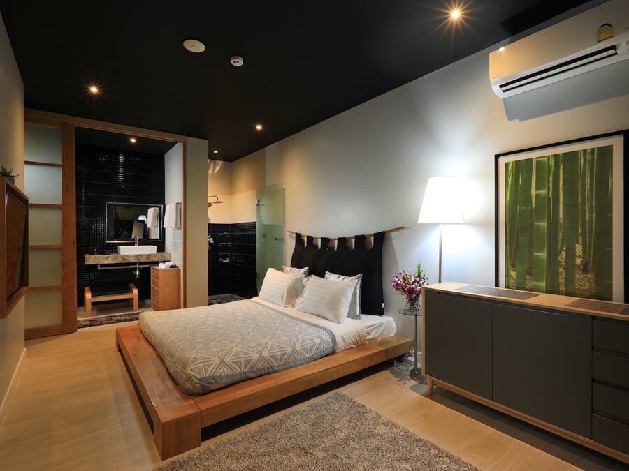 Un dormitorio moderno con una cama grande, una mesita de noche con lámpara, un armario y un baño visible a través de una puerta abierta.