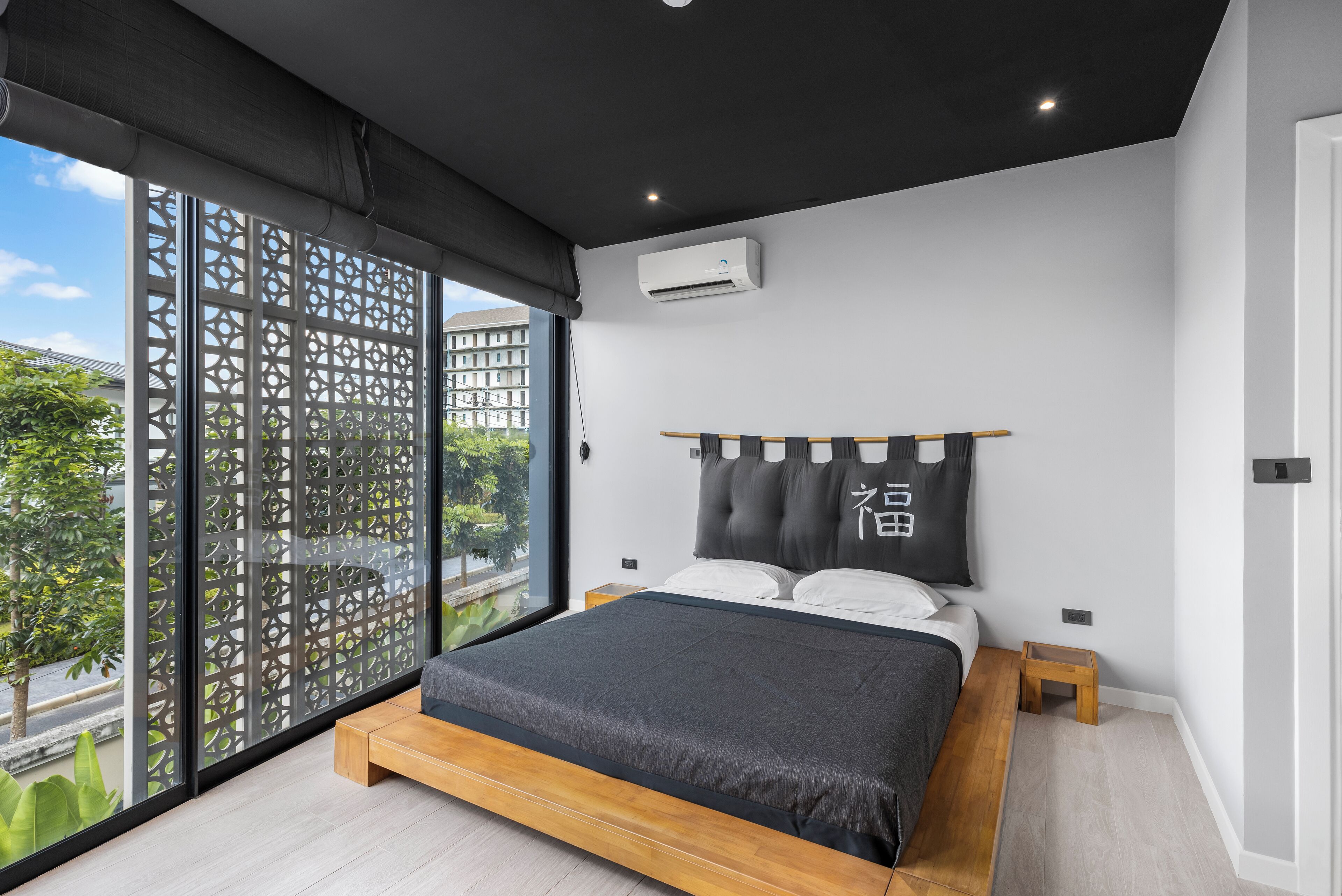 A modern bedroom with a large bed, a wooden headboard, and a view through a patterned window.