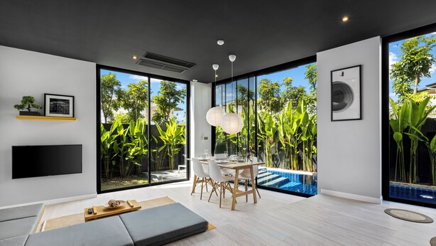 A modern living room with a dining area, large windows, and a pool view. - Villoft Zen Living (Choeng Thale)