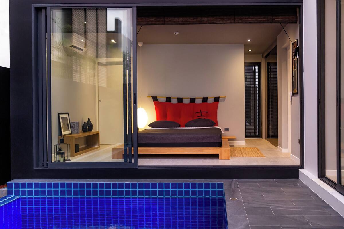 Un dormitorio moderno con una cama grande, una pared de acento roja y vistas a través de un ventanal.